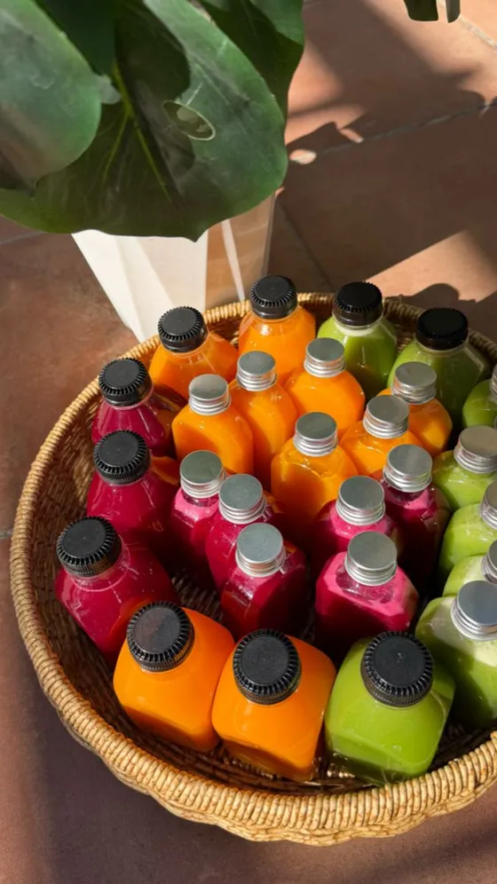 A basket of Eat Good Club wellness juices in bright pink, orange and green.